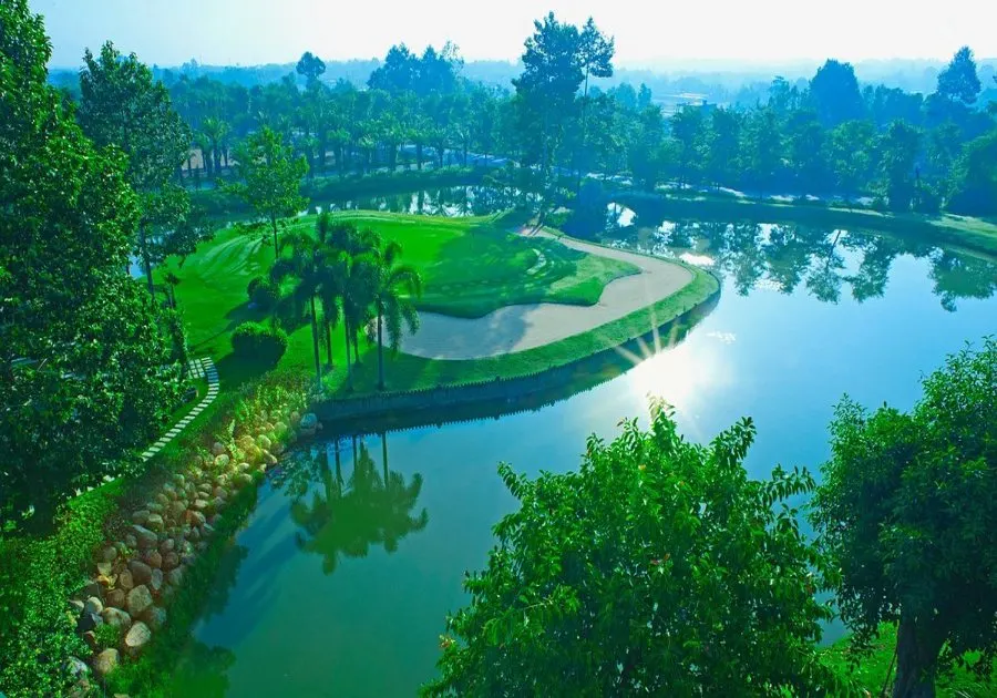 Image of a golf course driving range in Vietnam, featuring a spacious area with multiple hitting bays, well-maintained greens, practice targets, and golfers practicing their swings under clear skies.