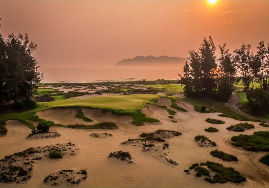 Image of a golf course driving range in Vietnam, featuring a spacious area with multiple hitting bays, well-maintained greens, practice targets, and golfers practicing their swings under clear skies.