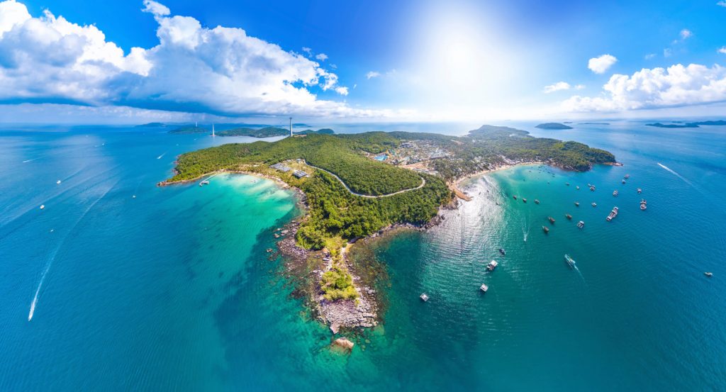 Idyllic scene of Phu Quoc Island with clear turquoise waters, white sandy beach, palm trees, and colorful coral reefs visible beneath the surface