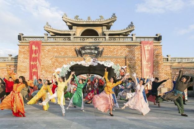 Visitors taking selfies at a picturesque spot in Hoi An Impression Theme Park, surrounded by lush greenery and traditional structures