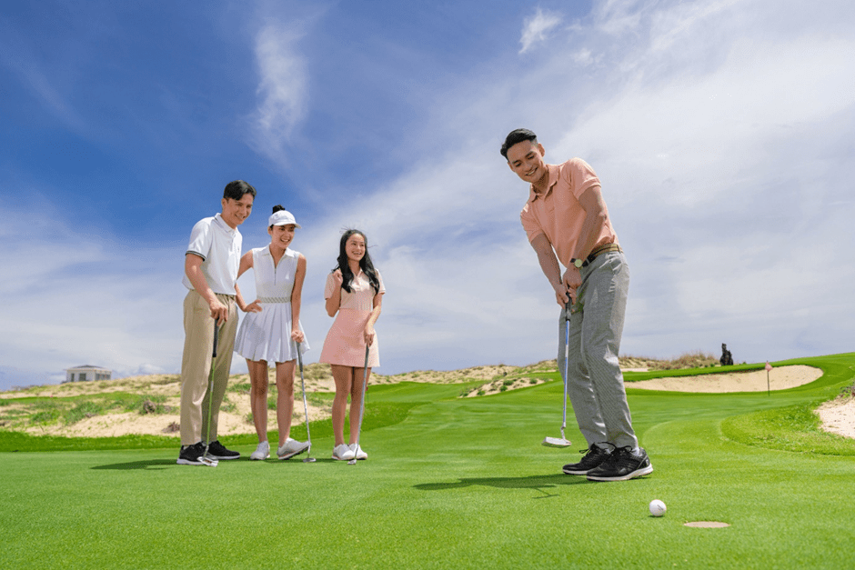 A family playing golf together on a green course in Vietnam, with parents guiding their children.