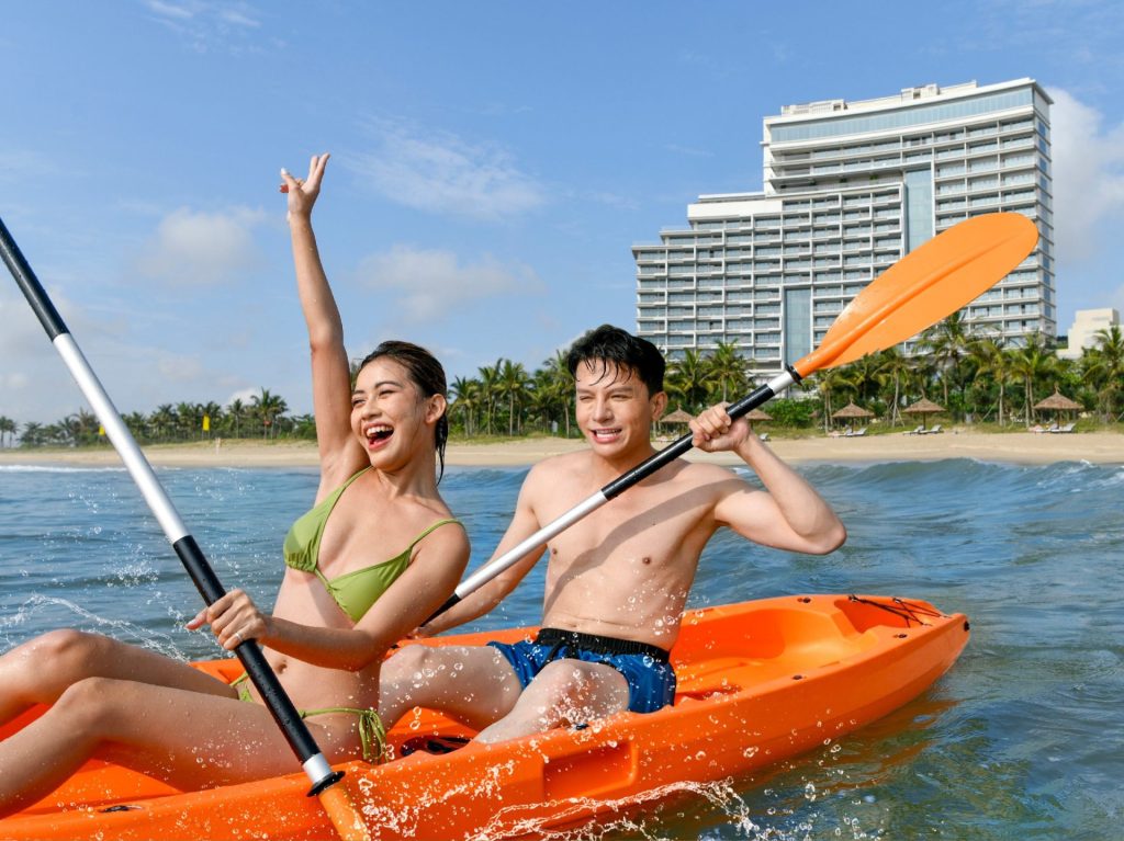 A family kayaking along the scenic coastline near Hoiana Resort & Golf, with the beach in the background.