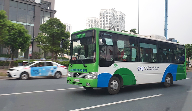 A bus on a rural road in Vietnam, with a car driving alongside through lush greenery.