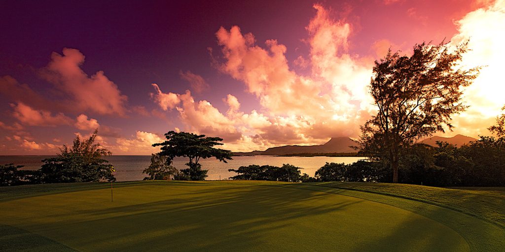 Golfers walking down the fairway at dusk, with the sky glowing orange and pink.