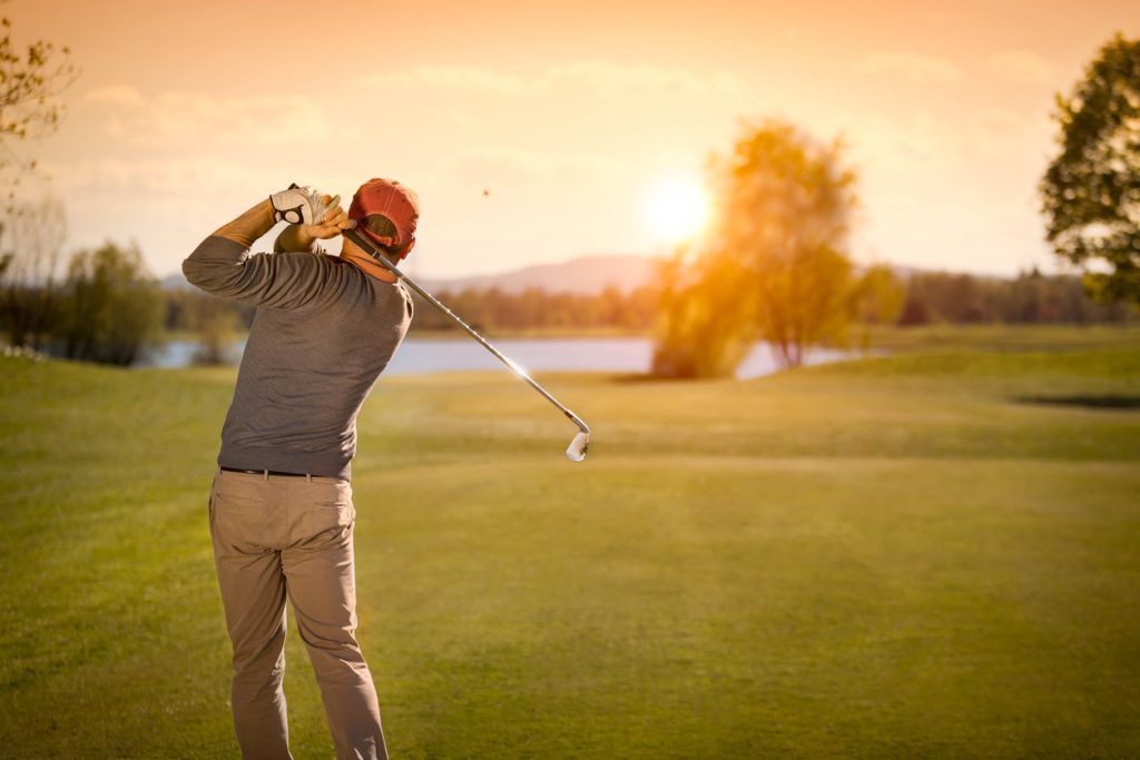 A golfer teeing off under a colorful twilight sky, with soft lighting across the golf course.