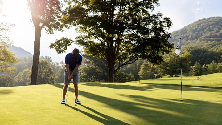 A golfer dressed in light, comfortable attire appropriate for an evening round of golf.