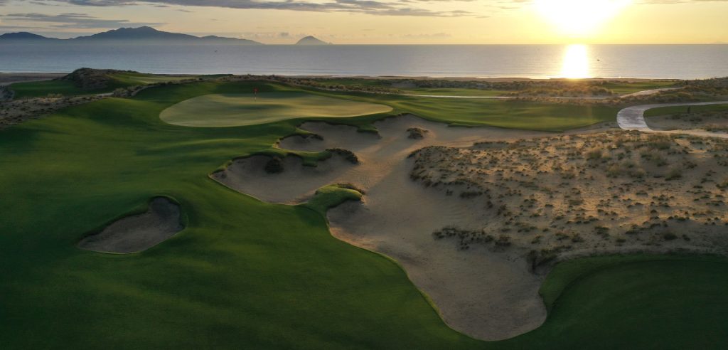 A picturesque view of Hoiana Shores Golf Club at twilight, with the course softly lit and the ocean in the background.