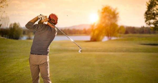 A golfer teeing off under a colorful twilight sky, with soft lighting across the golf course.