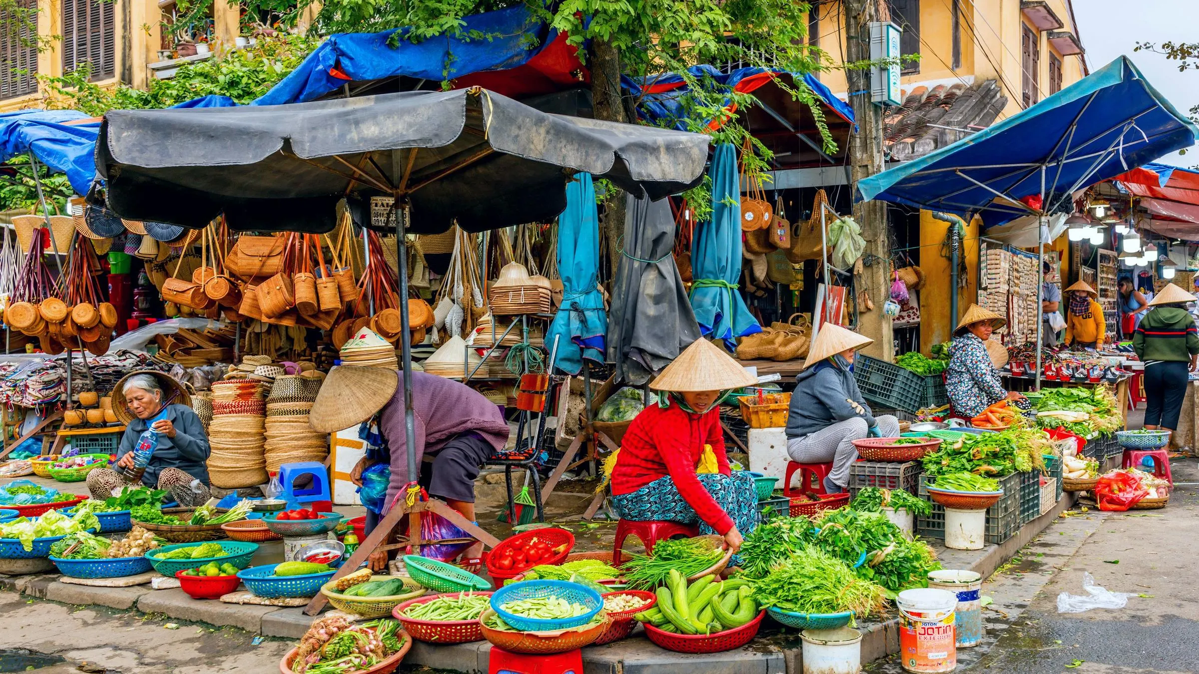 A close-up of a vendor at Hoi An Market offering colorful lanterns, textiles, and local spices to customers.