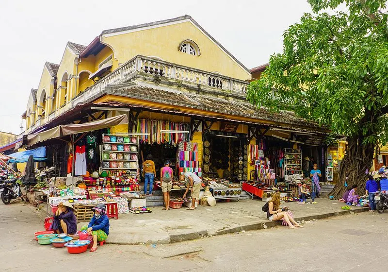 A bustling scene at Hoi An Market with vendors selling traditional Vietnamese foods, souvenirs, and handmade goods.