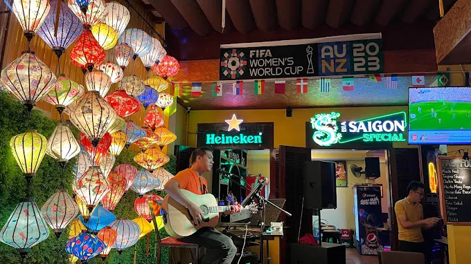 Interior view of a trendy bar in Hoi An, showcasing vibrant décor, cocktails on the counter, and guests enjoying a relaxing evening atmosphere.