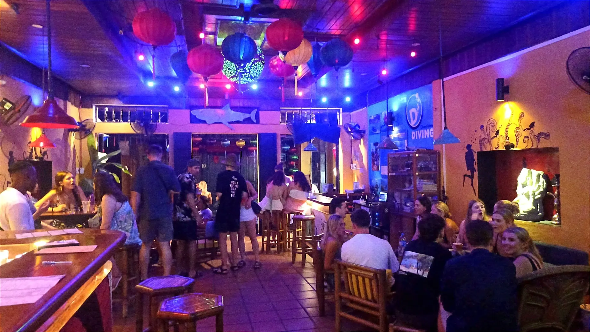 Interior view of a trendy bar in Hoi An, showcasing vibrant décor, cocktails on the counter, and guests enjoying a relaxing evening atmosphere.