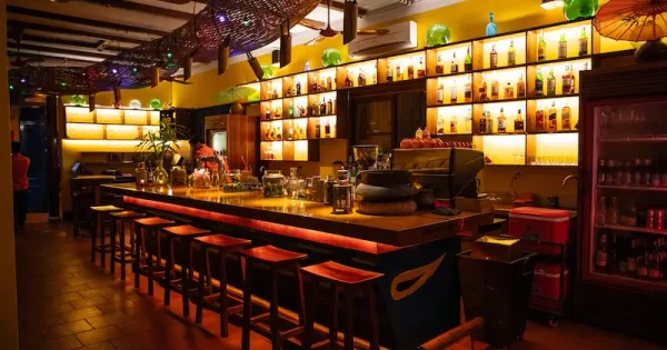 Interior view of a trendy bar in Hoi An, showcasing vibrant décor, cocktails on the counter, and guests enjoying a relaxing evening atmosphere.