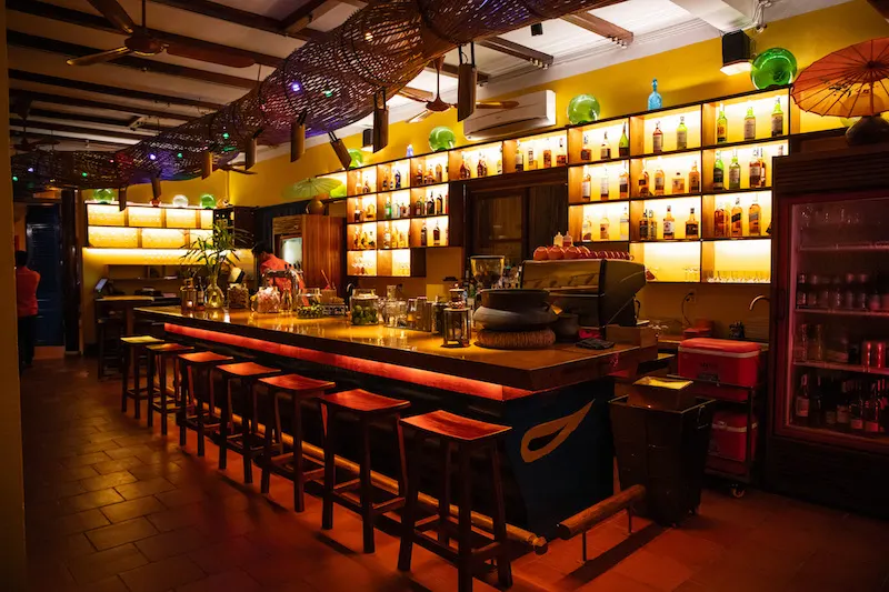 Interior view of a trendy bar in Hoi An, showcasing vibrant décor, cocktails on the counter, and guests enjoying a relaxing evening atmosphere.