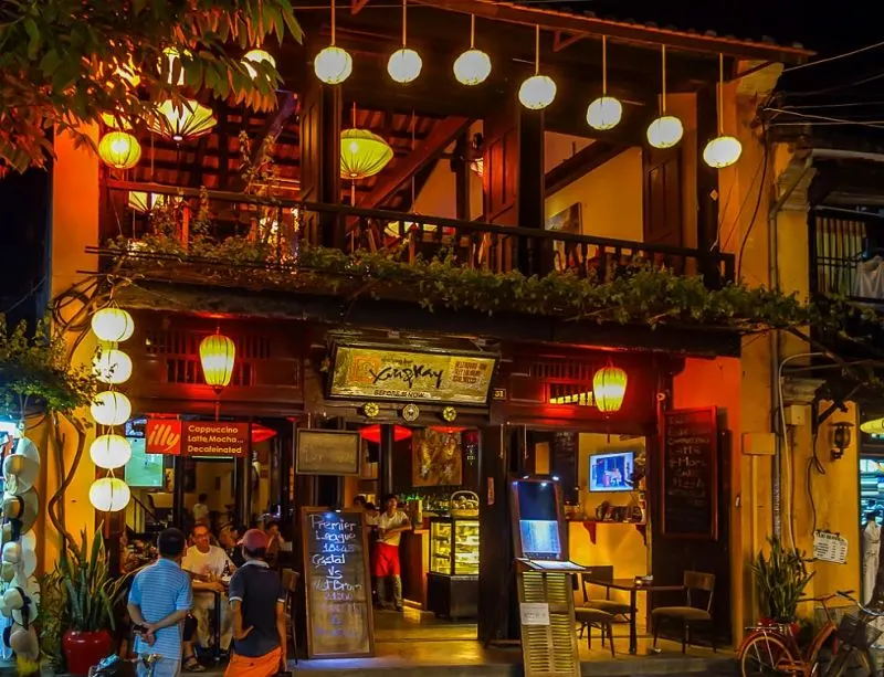 Interior view of a trendy bar in Hoi An, showcasing vibrant décor, cocktails on the counter, and guests enjoying a relaxing evening atmosphere.