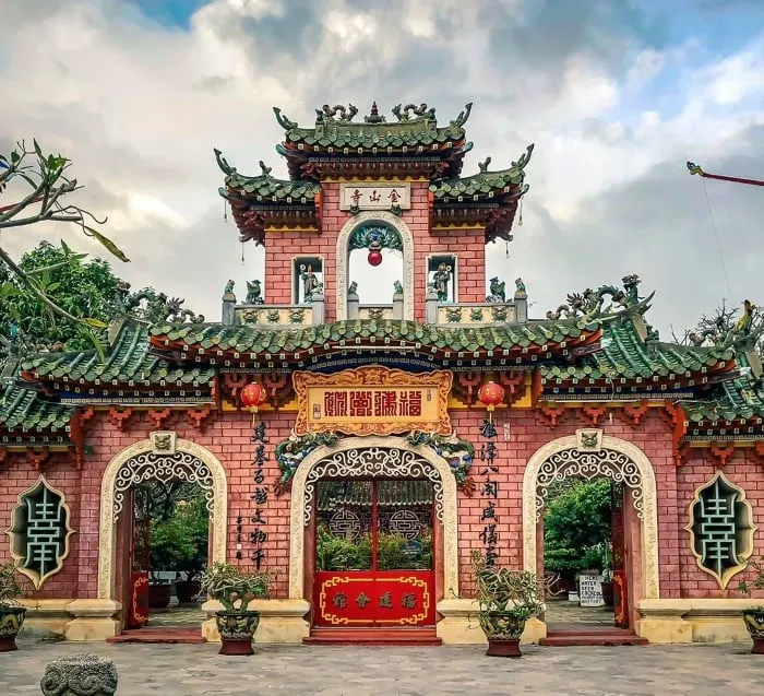 Scenic view of Hoi An in January, with peaceful streets lined with traditional yellow-tinted buildings, lanterns glowing softly in the cool winter evening. The riverside is calm, reflecting the warm hues of sunset, and locals and tourists wander through the charming, historic town under clear blue skies.