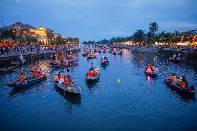 Scenic view of Hoi An in January, with peaceful streets lined with traditional yellow-tinted buildings, lanterns glowing softly in the cool winter evening. The riverside is calm, reflecting the warm hues of sunset, and locals and tourists wander through the charming, historic town under clear blue skies.