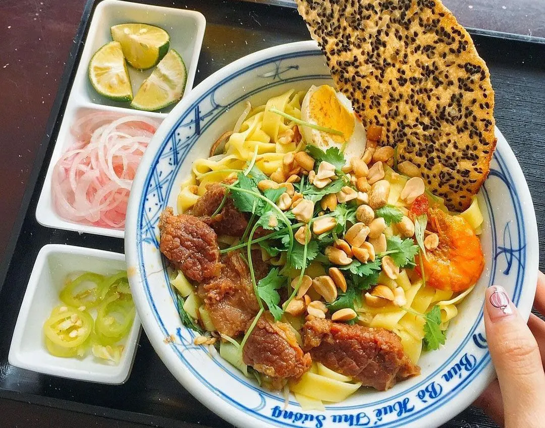 "꽝 국수: 고소하고 깊은 맛이 나는 국물과 함께 쫄깃한 면이 특징인 베트남 전통 국수 요리. 다양한 고명과 함께 제공되어 풍미를 더함."