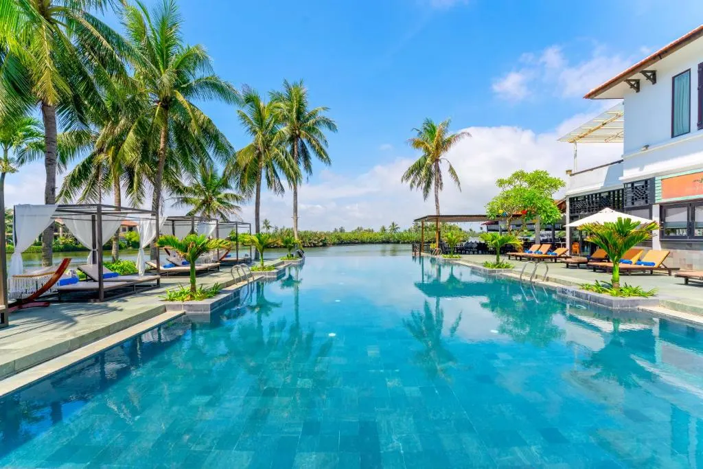 Ảnh chụp một **resort Hội An giá tốt** với kiến trúc truyền thống, bao quanh bởi cây xanh và hồ bơi trong xanh, mang đến không gian nghỉ dưỡng thoải mái và thư giãn.